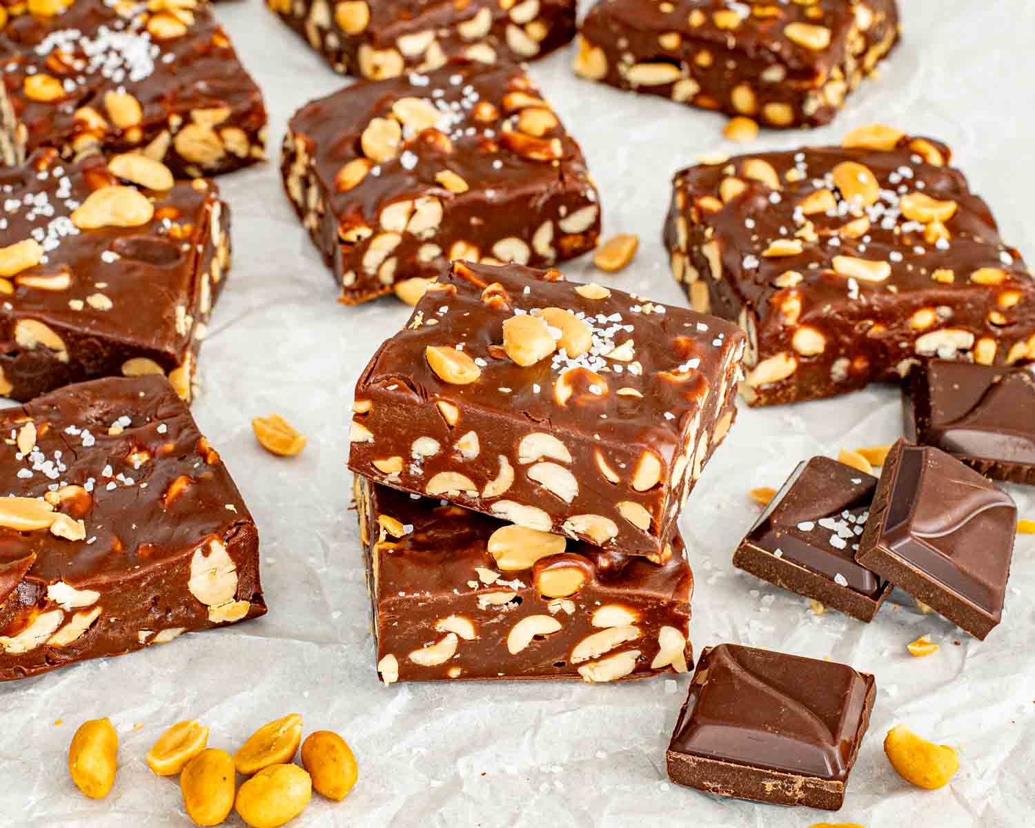 Stacked homemade chocolate peanut bars showing a dense and chewy center filled with many whole roasted peanuts.