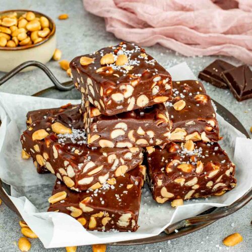 A pile of chewy chocolate peanut bars on parchment paper inside a rustic metal tray with salt.