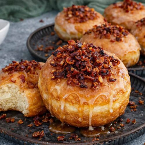 High angle shot of several golden yeast donuts topped with a thick maple glaze and a pile of crispy bacon.