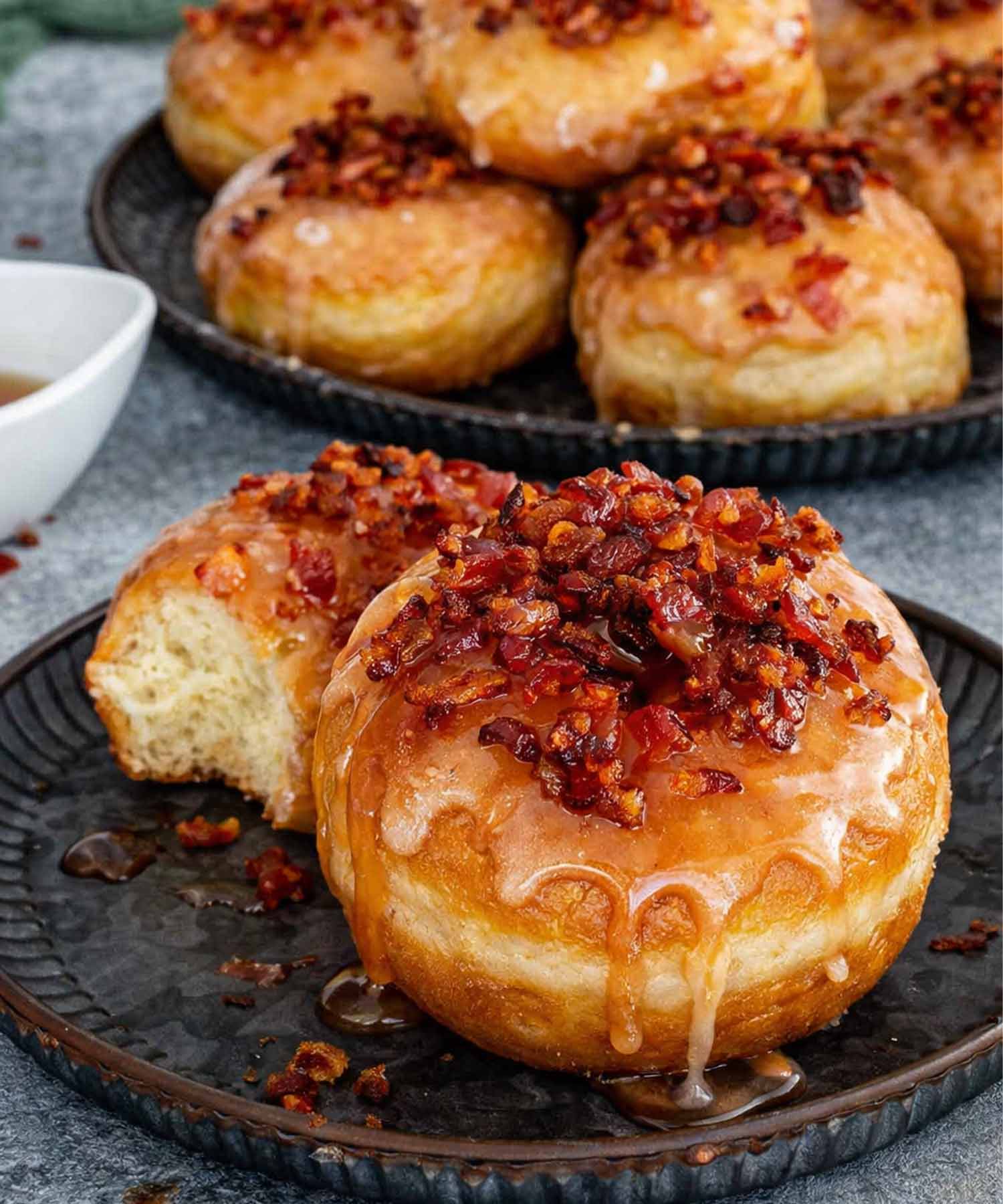 Close up of a fluffy maple glazed donut with crispy bacon topping and one donut with a bite taken.
