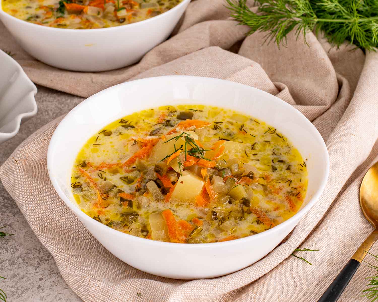 Homemade dill pickle soup with potatoes, carrots, chopped pickles, and herbs served in white bowl on rustic linen background.