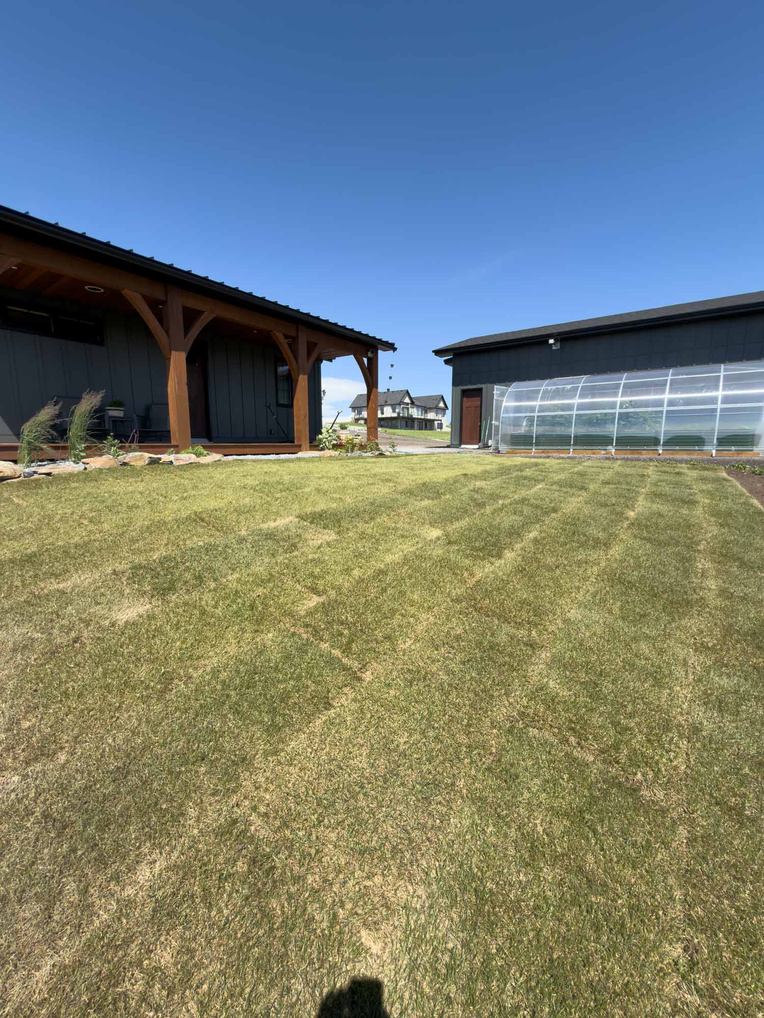 Modern black garden studio with covered porch, curved walkway, and green lawn under bright summer skies on rural acreage.