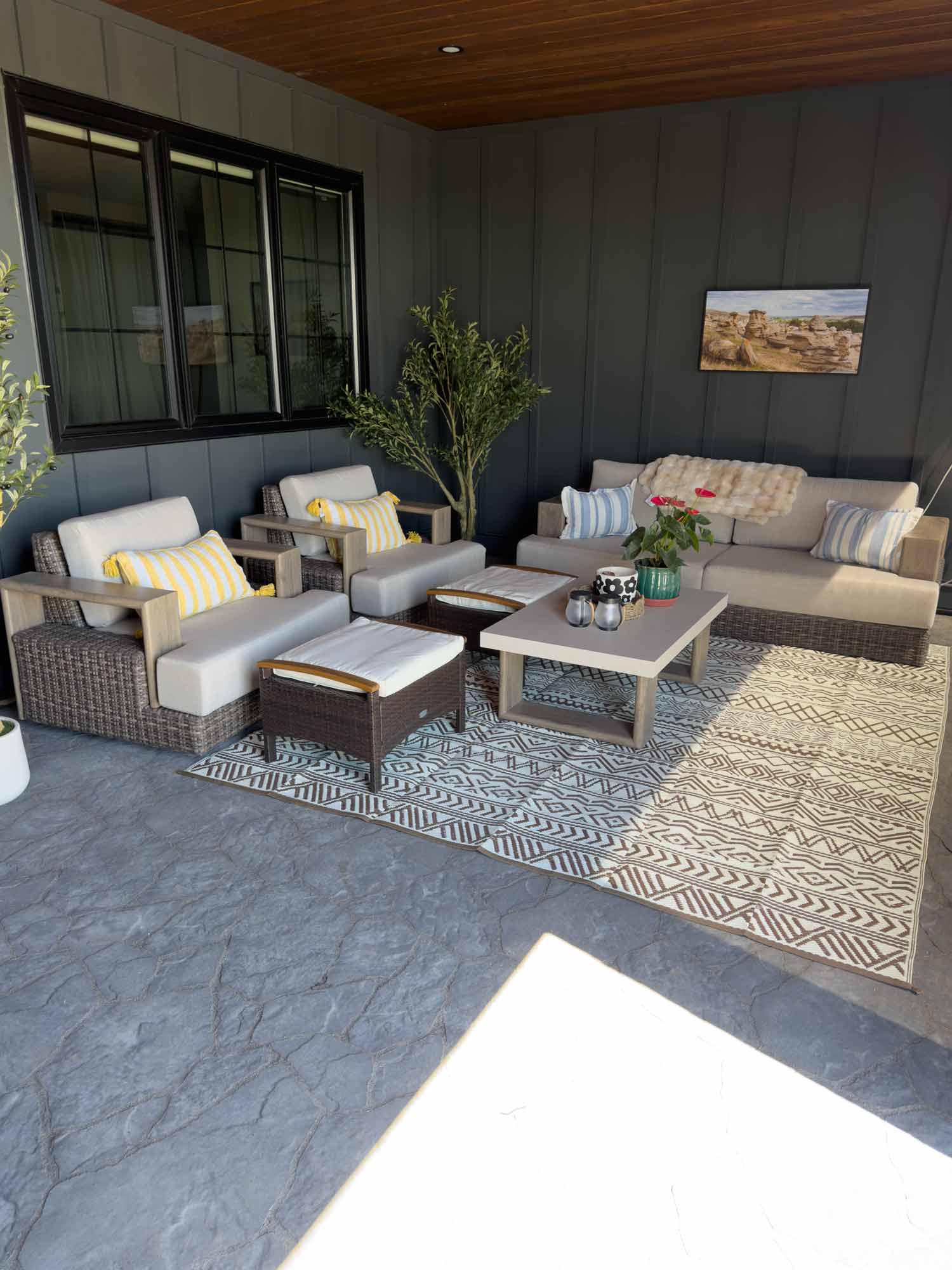 Covered outdoor living space with retractable screen, comfortable seating, patterned rug, and peaceful lawn views beyond the enclosed patio.