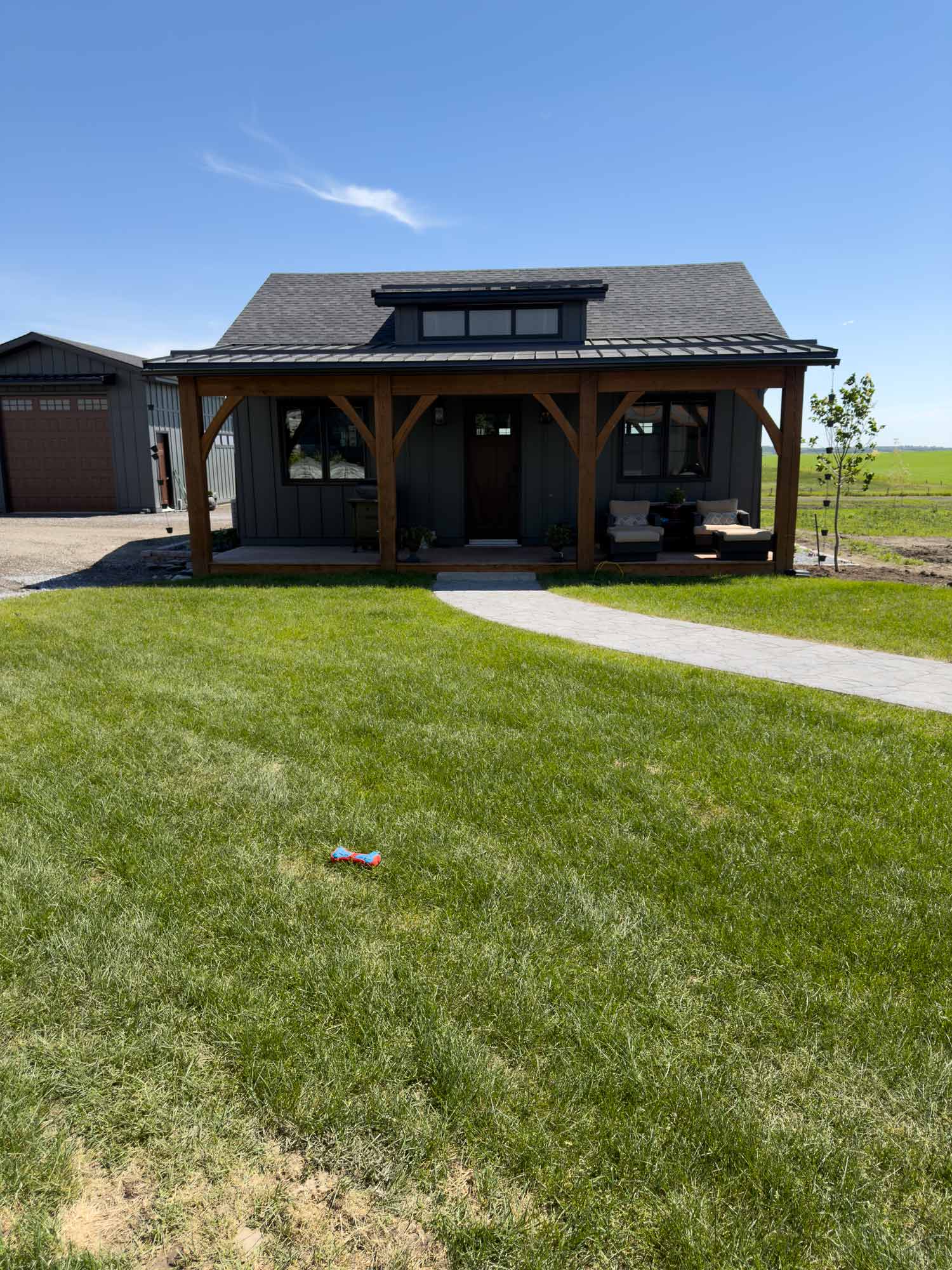 Cozy covered patio with outdoor sofa, chairs, patterned rug, coffee table, and dark modern farmhouse exterior in soft shade.
