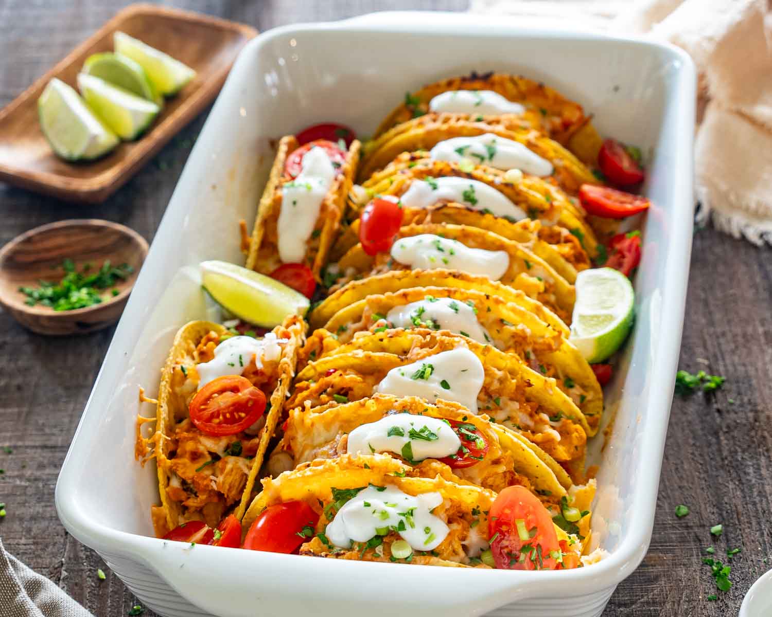 Cheesy baked chicken tacos topped with sour cream and fresh herbs, served in a white casserole dish.