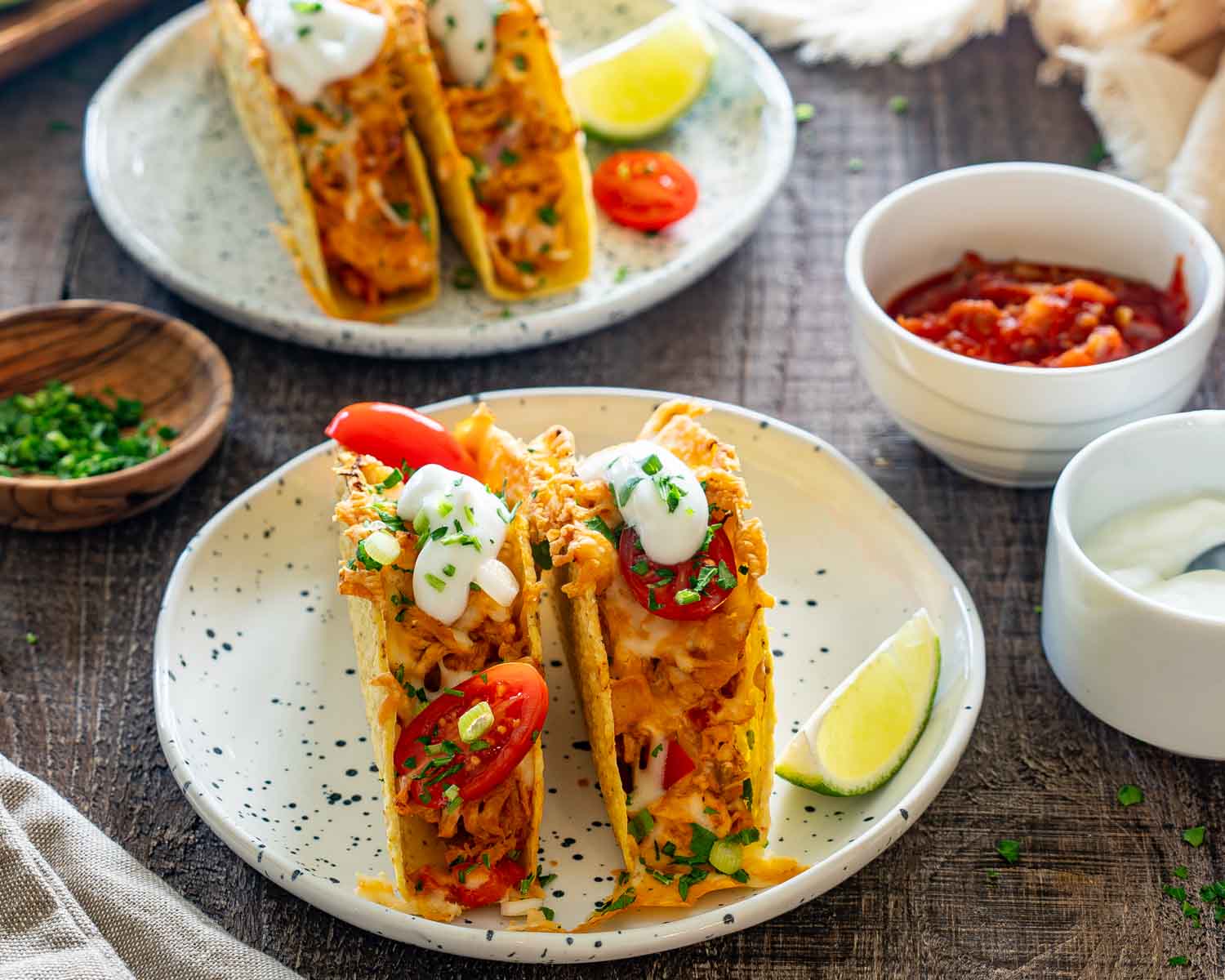 Two cheesy baked chicken tacos served on a speckled plate with sour cream, lime wedge, and salsa.