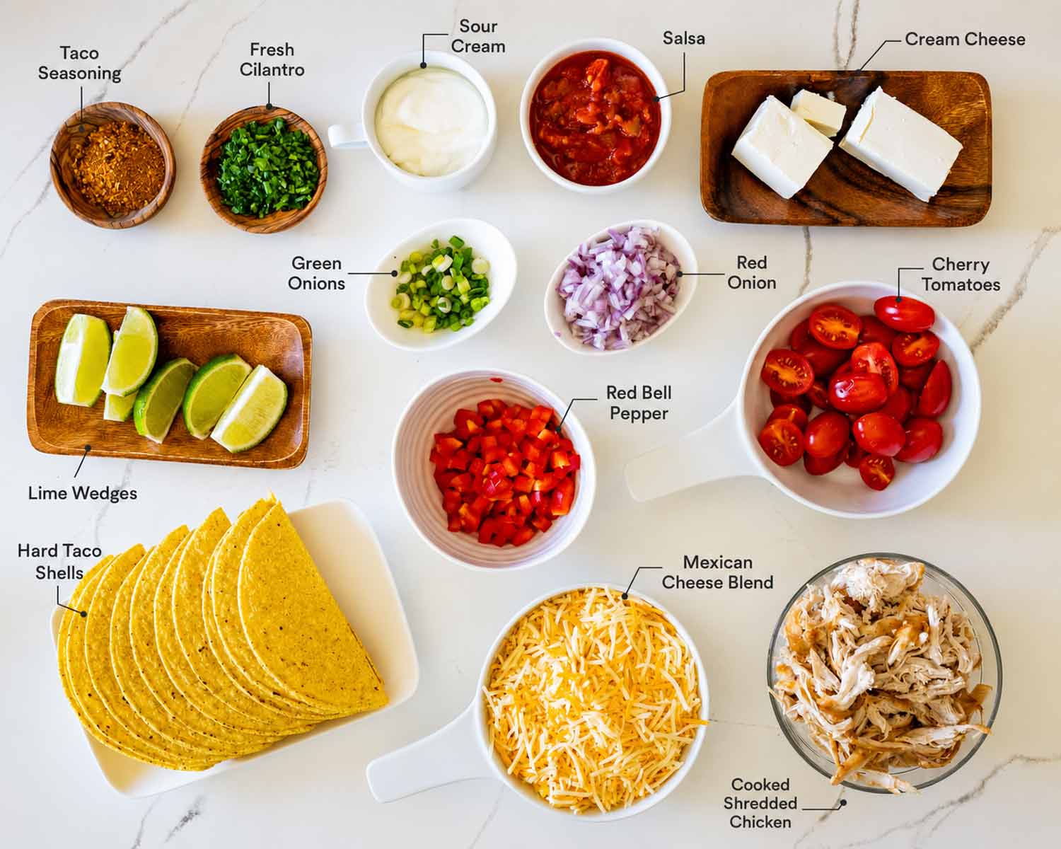 Ingredients for cheesy baked chicken tacos arranged in labeled bowls, including chicken, cheese, salsa, vegetables, and toppings.