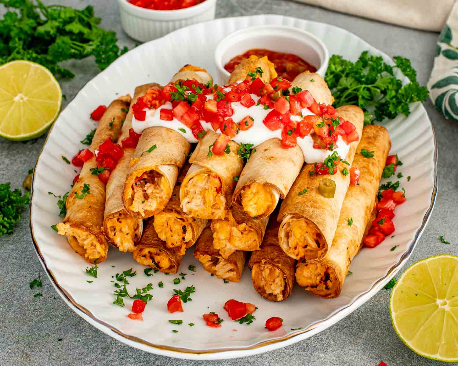 Crispy baked chicken taquitos topped with sour cream and fresh pico de gallo served with salsa and lime wedges.