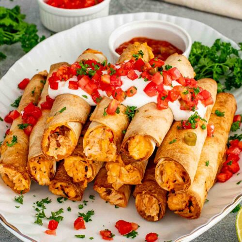 Platter of crispy chicken taquitos topped with sour cream, pico de gallo, jalapeños, fresh parsley, and chunky salsa.