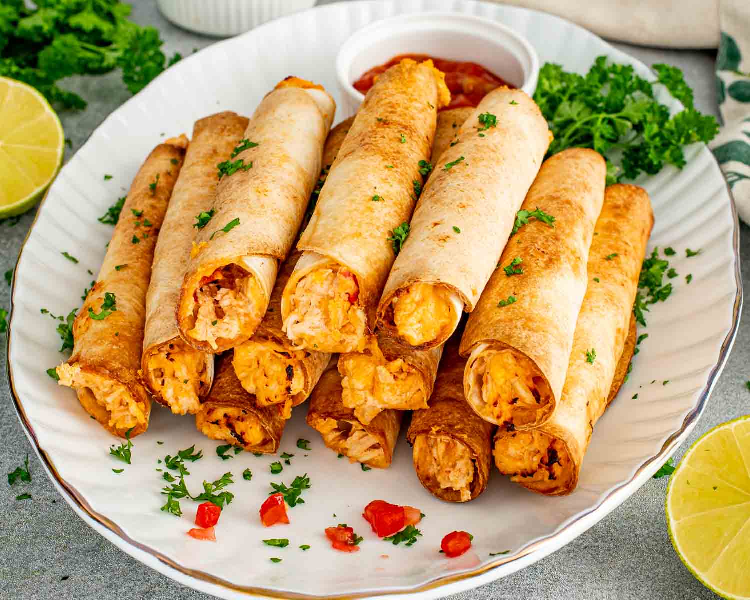 Crispy baked chicken taquitos stacked on a platter with golden tortillas, shredded chicken filling, parsley, salsa, and fresh lime.