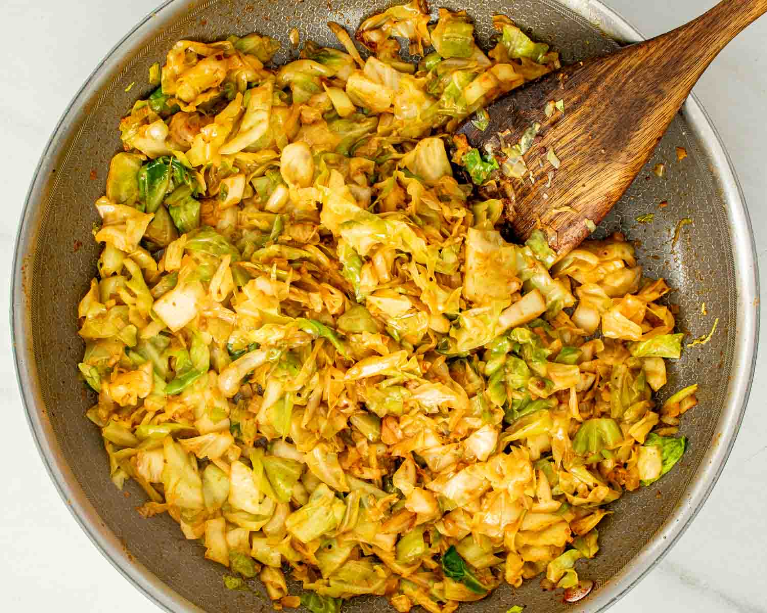 Overhead view of fried cabbage with crispy bacon and browned sausage slices cooked together in a large skillet.