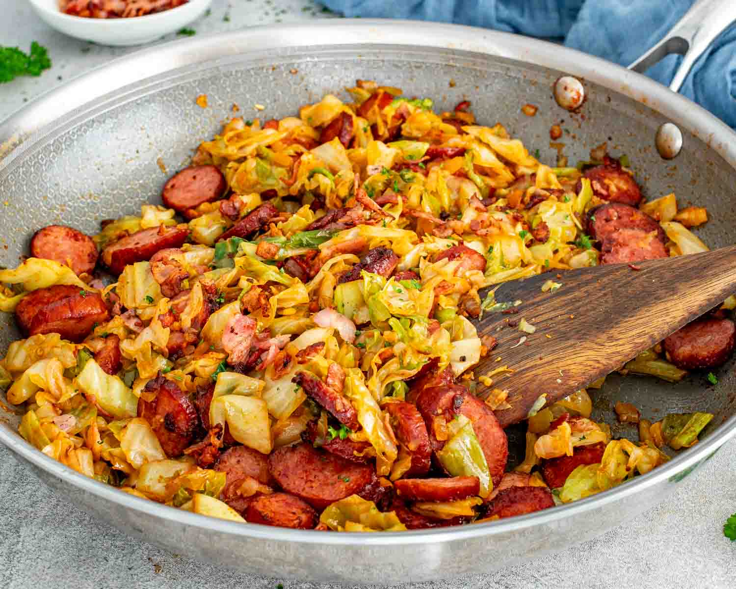 Close-up skillet view of fried cabbage tossed with crispy bacon and browned sausage slices for an easy dinner.