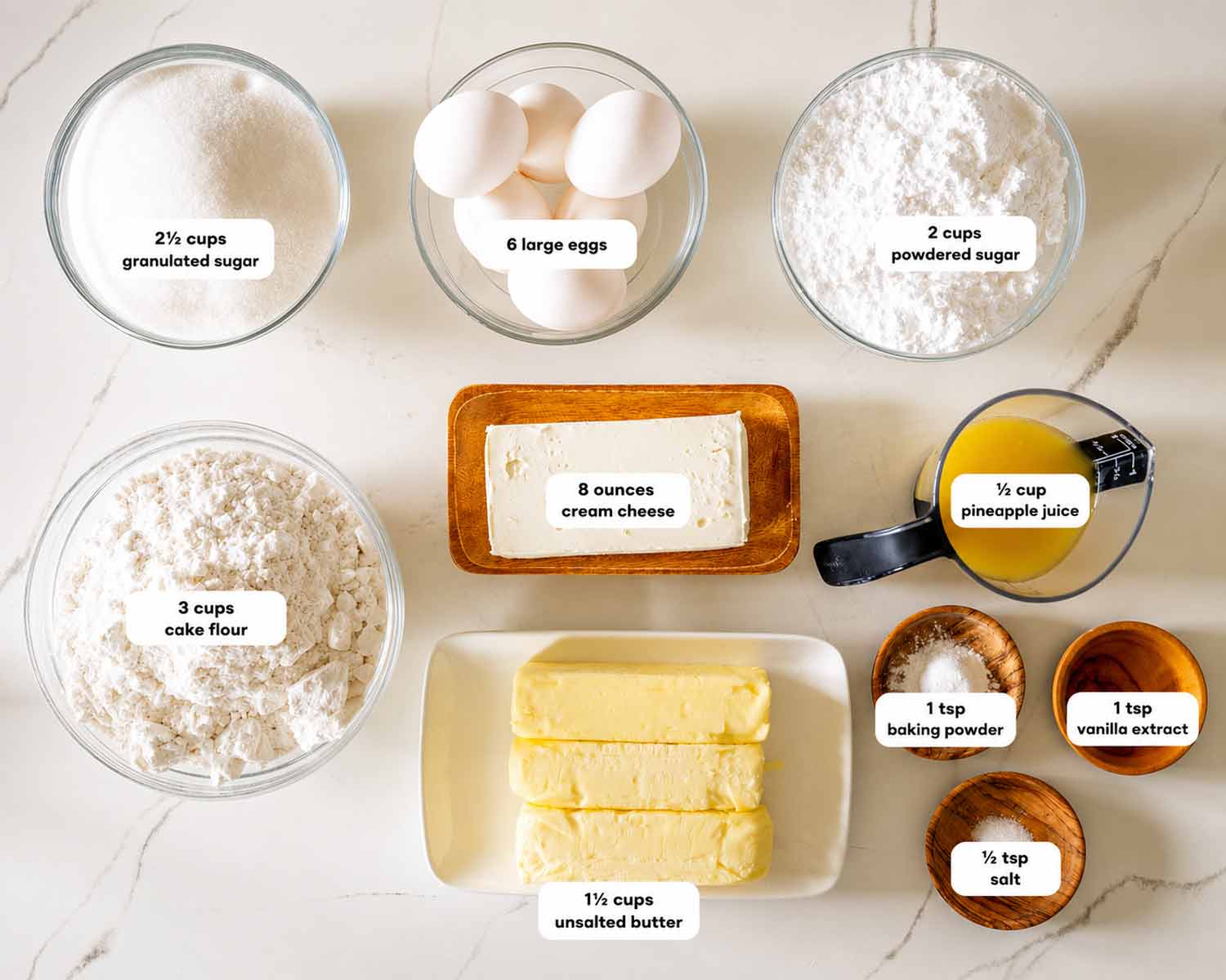 Ingredients for pineapple cream cheese pound cake arranged neatly, including butter, cream cheese, eggs, sugar, flour, and juice.