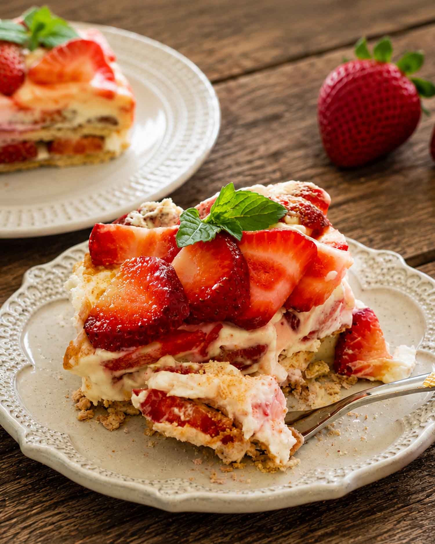 Close up plated slice of no bake strawberry icebox cake topped with fresh strawberries and mint on vintage plate.
