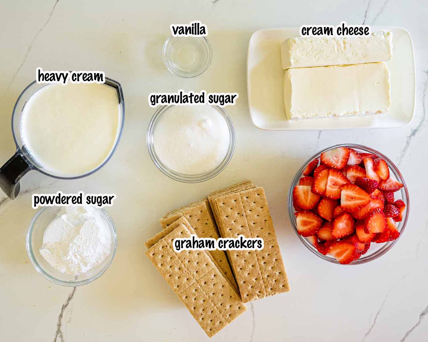 Overhead ingredient shot showing cream cheese, heavy cream, graham crackers, strawberries, vanilla, and sugars for strawberry icebox cake.