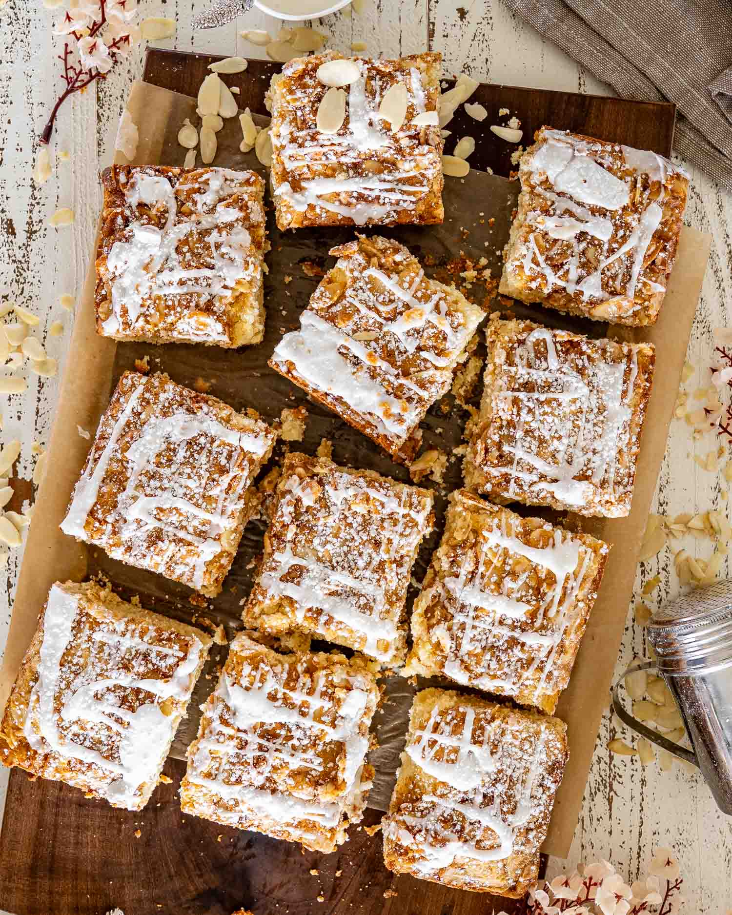 Freshly baked almond croissant bars in a parchment-lined pan, generously dusted with powdered sugar and finished with vanilla icing drizzle.