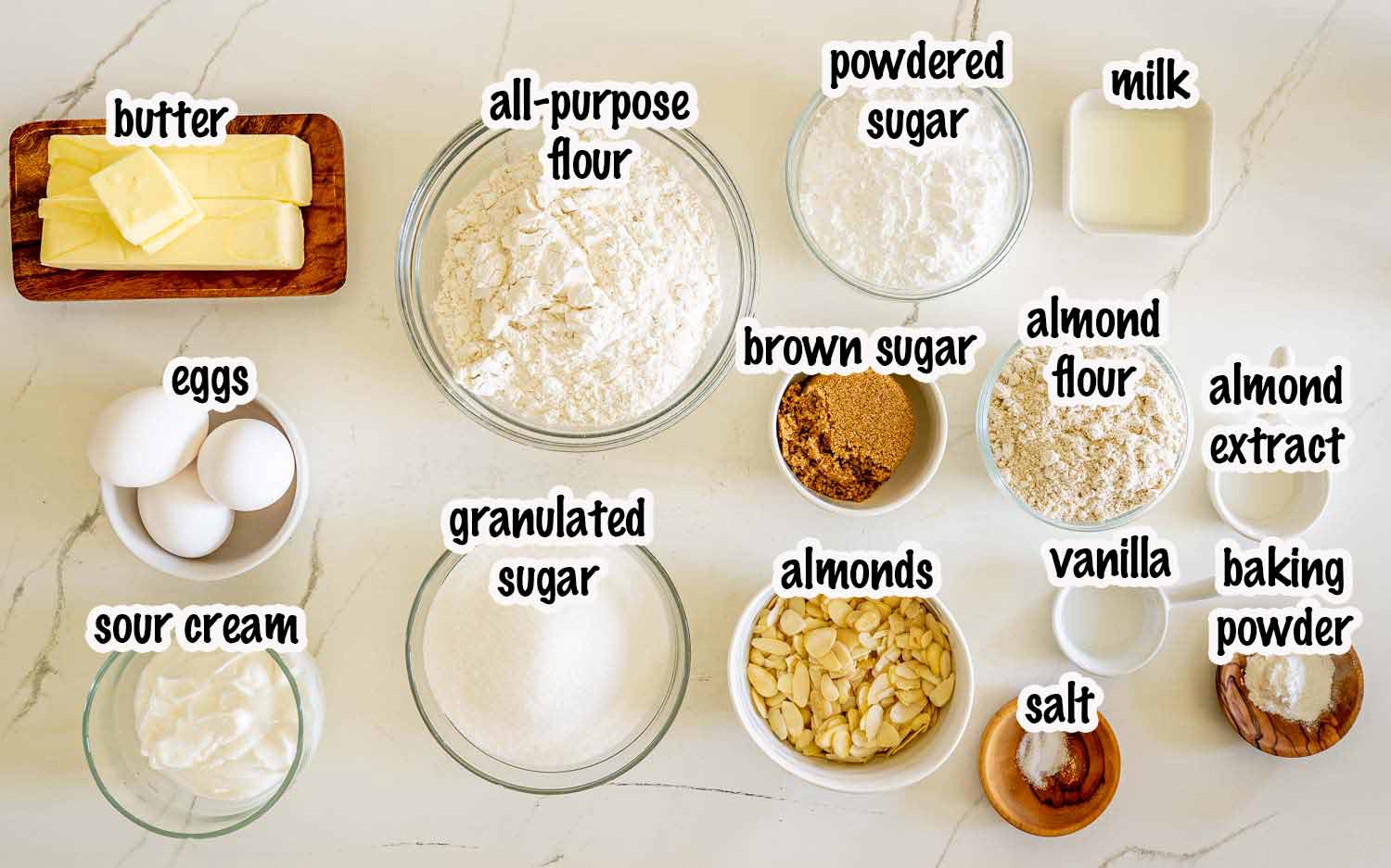 Overhead view of ingredients for almond croissant bars including butter, flour, eggs, sour cream, almonds, sugars, and almond extract.