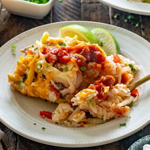 Chicken fajita rice casserole topped with salsa and cilantro, served on a plate with lime wedges and a fork.