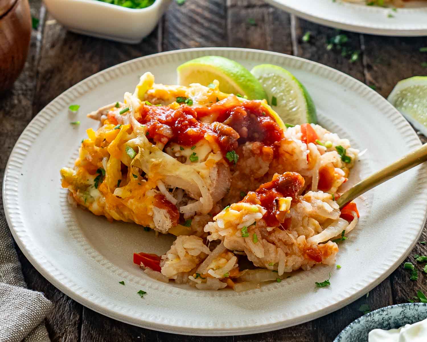 Chicken fajita rice casserole topped with salsa and cilantro, served on a plate with lime wedges and a fork.