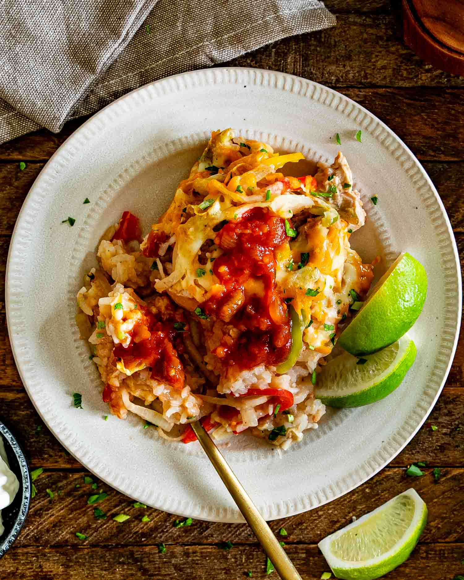 Overhead serving of chicken fajita rice casserole topped with salsa and cilantro, plated with fresh lime wedges.