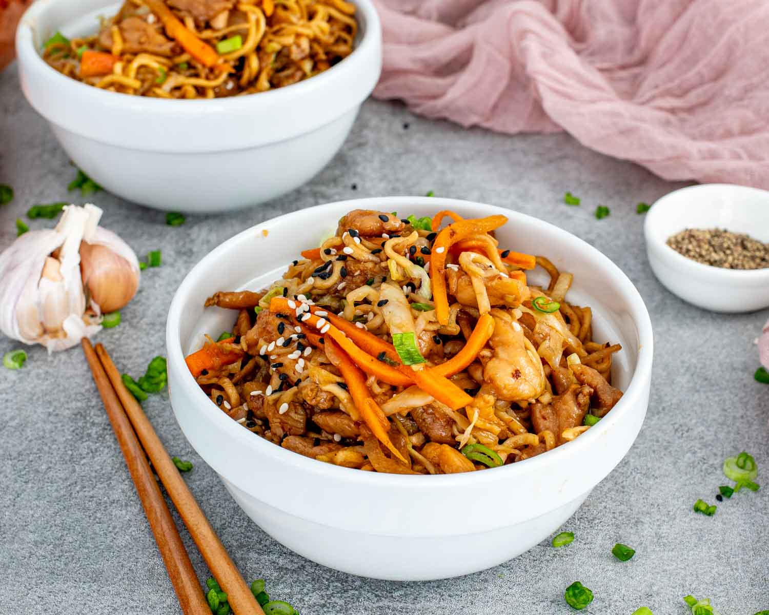 Chicken noodle stir fry served in a shallow bowl with juicy chicken, cabbage, carrots, and glossy noodles sprinkled with sesame seeds.