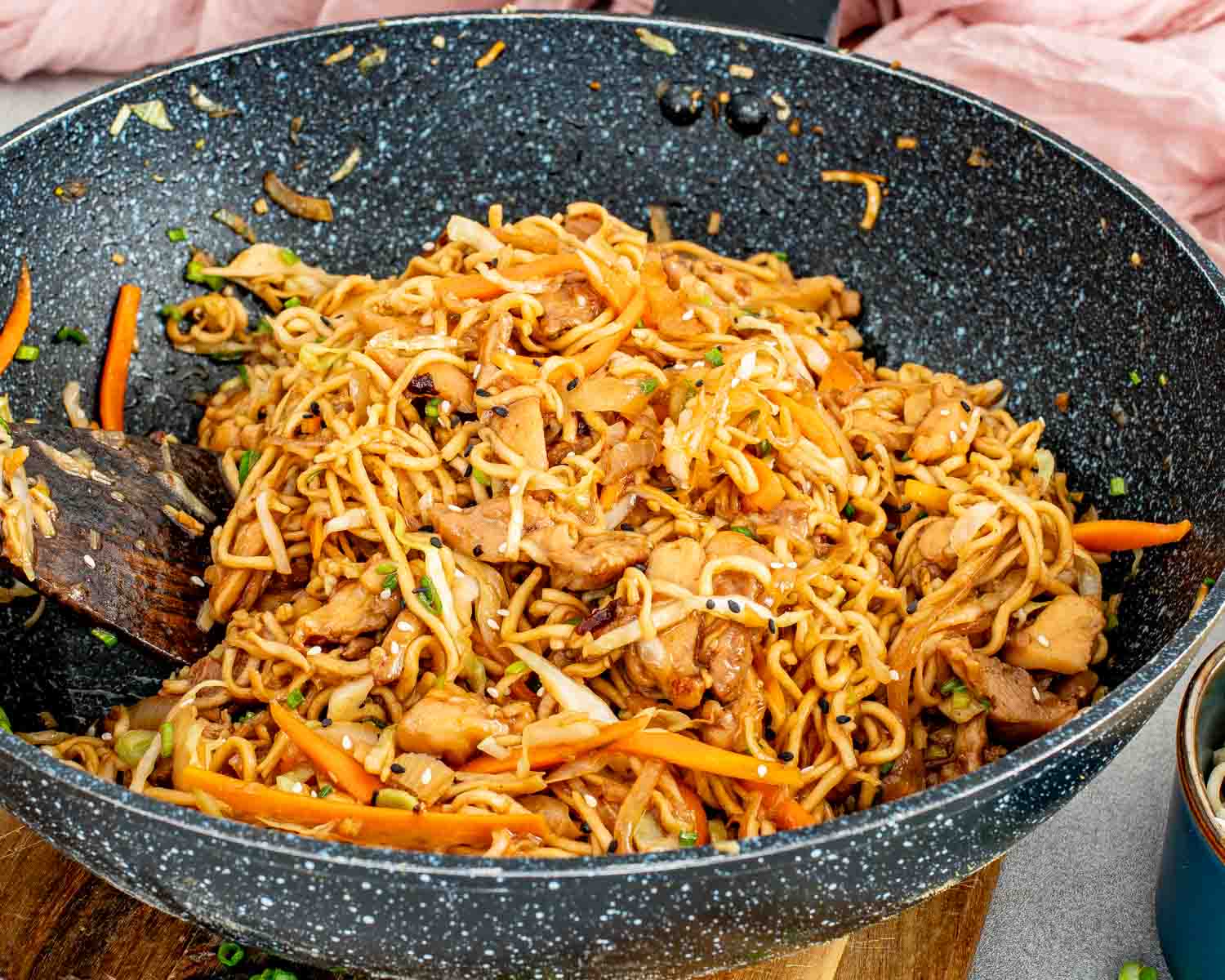 Side view of chicken noodle stir fry piled high in a skillet with juicy chicken, cabbage, carrots, and flavorful noodles.