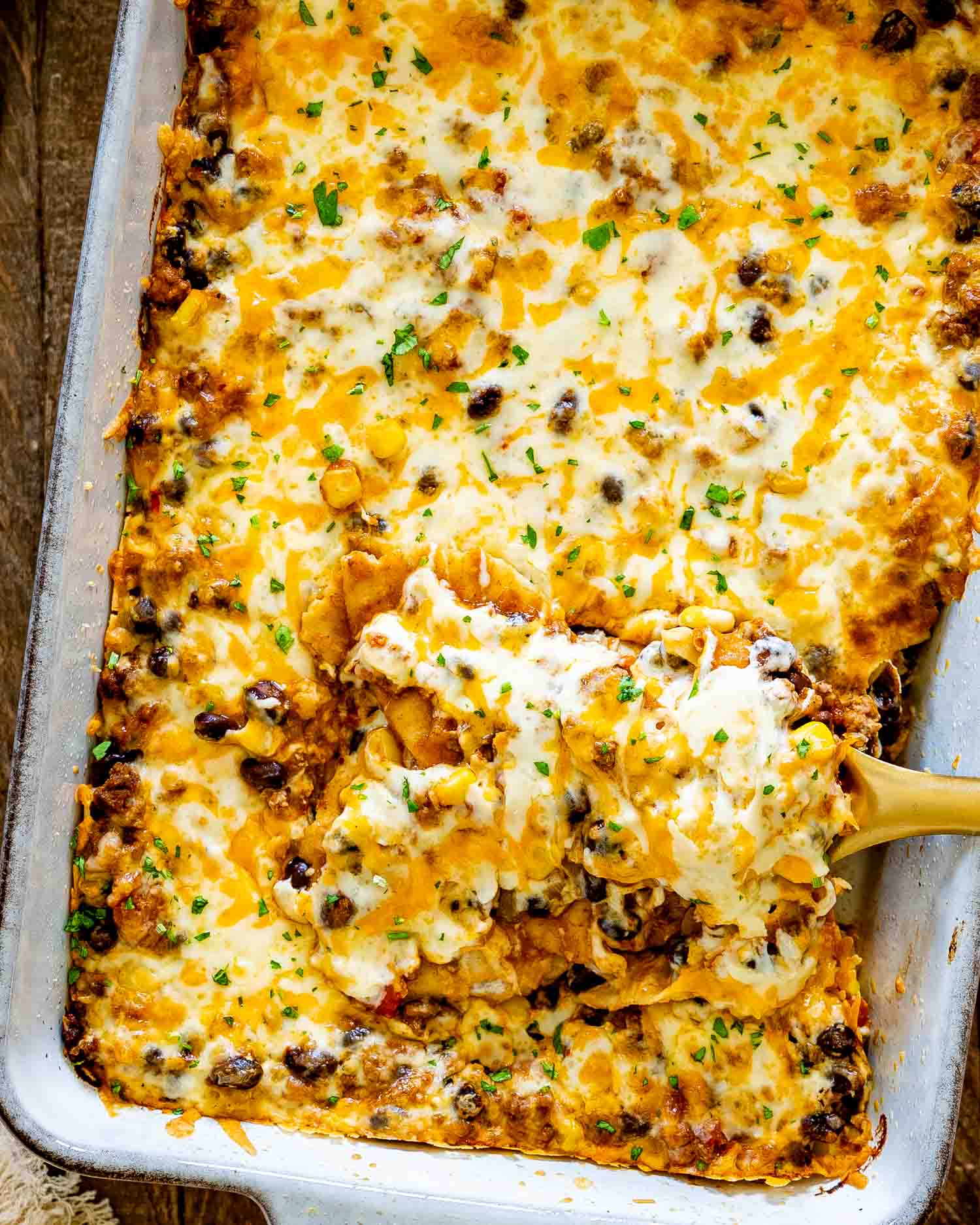 Overhead view of cheesy Tex-Mex beef enchilada casserole with one generous serving being scooped from the baking dish.