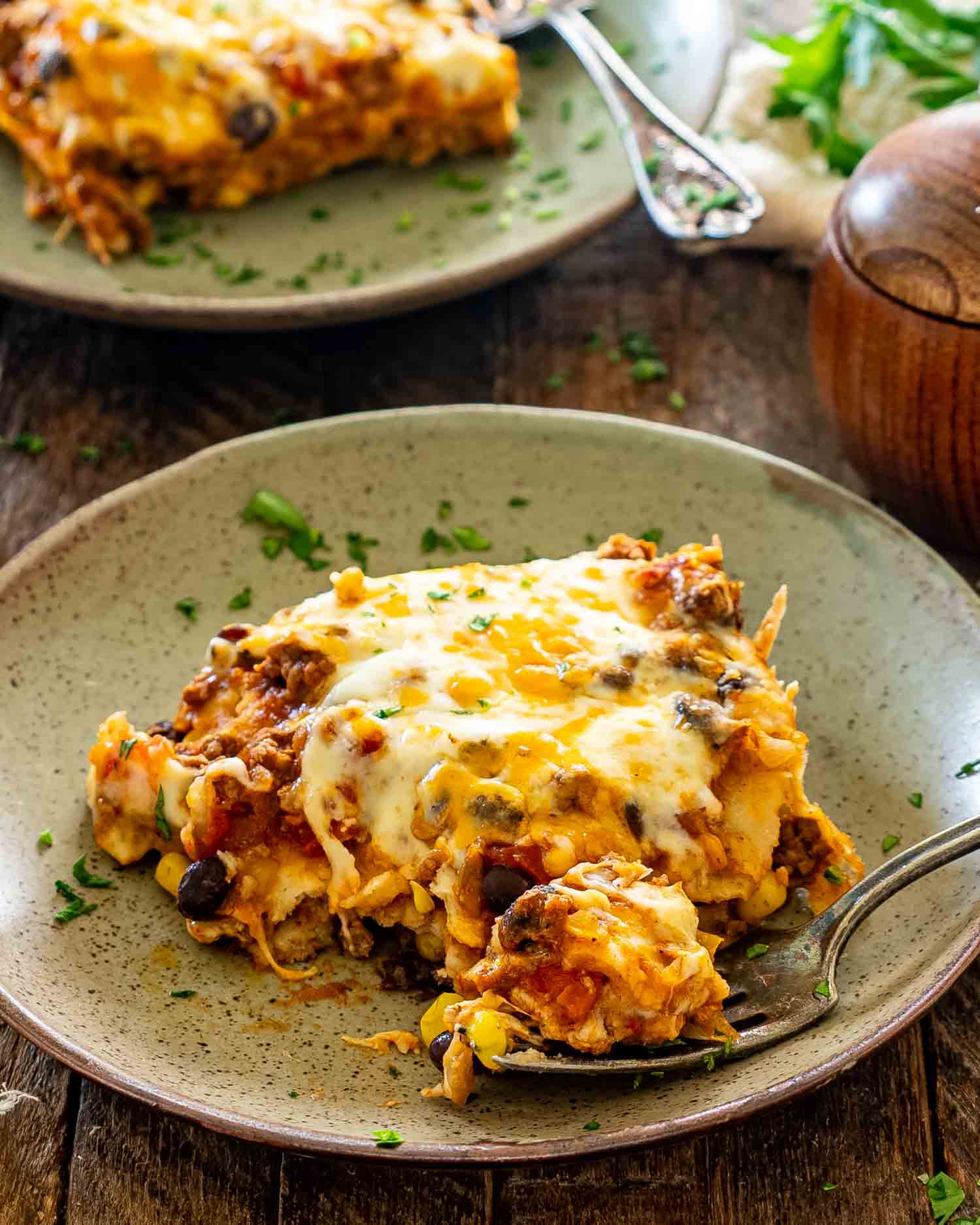 Close-up of cheesy Tex-Mex beef enchilada casserole on a plate, with a spoonful of beef, beans, and corn.