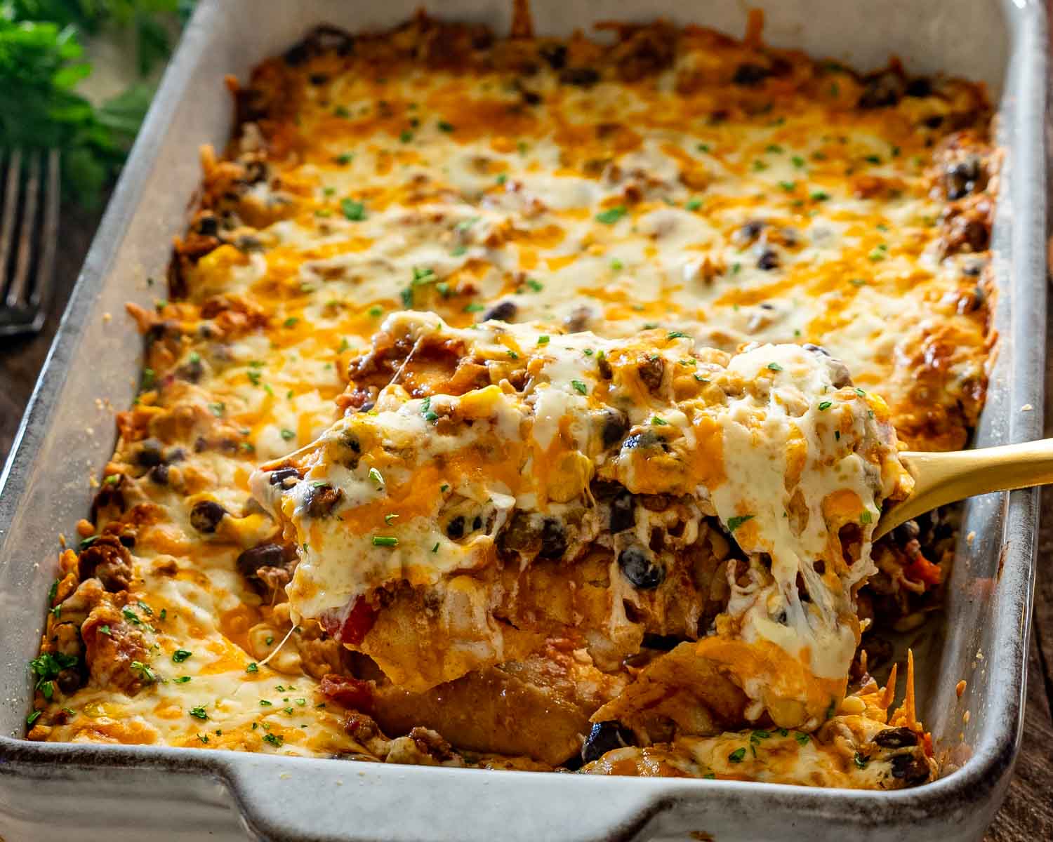 Hearty Tex-Mex beef enchilada casserole lifted from the baking dish, revealing layers of tortillas, seasoned beef, beans, and cheese.