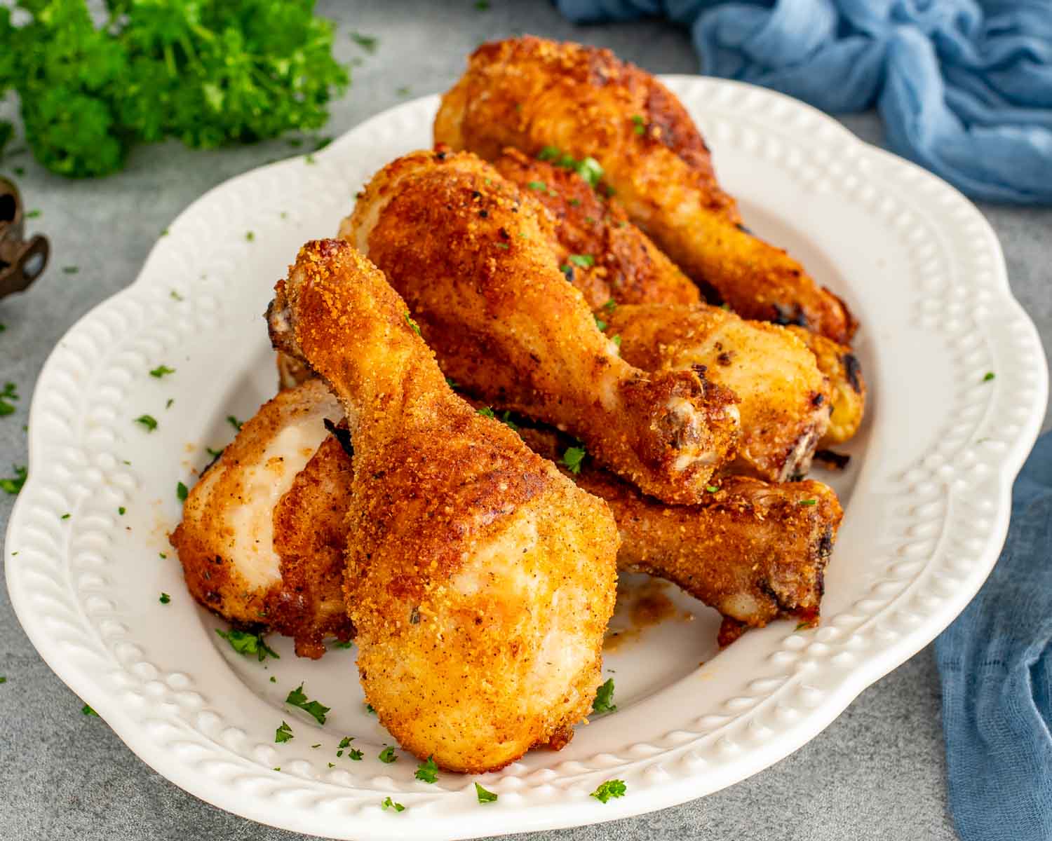 Close-up of crispy Air Fryer Shake-and-Bake Chicken drumsticks piled on a serving platter with golden, crunchy homemade breadcrumb coating.