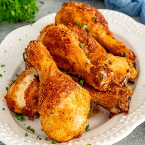 Close-up of crispy Air Fryer Shake-and-Bake Chicken drumsticks piled on a serving platter with golden, crunchy homemade breadcrumb coating.