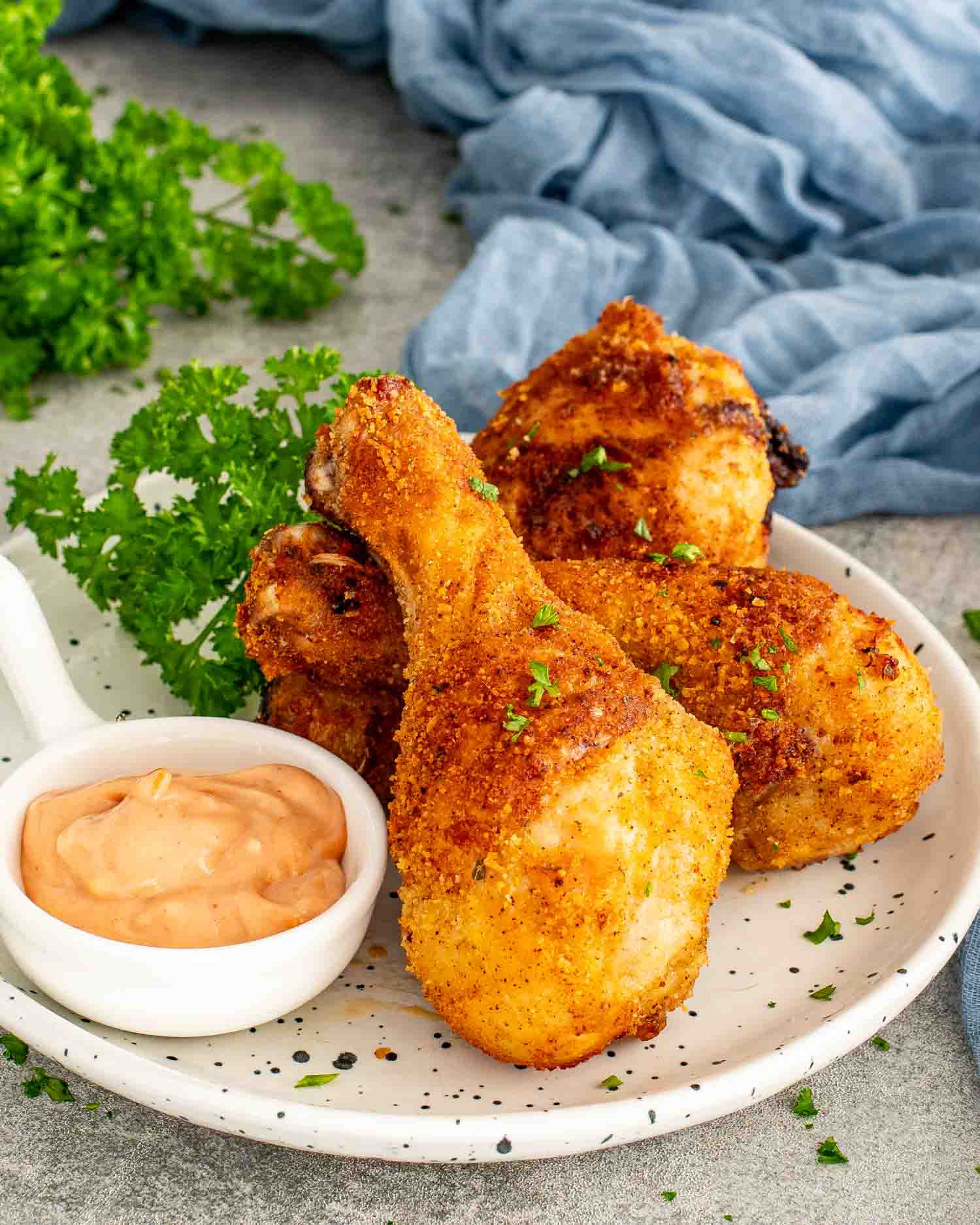 Golden Air Fryer Shake-and-Bake Chicken drumsticks served with creamy dipping sauce, garnished with parsley for an easy family dinner.