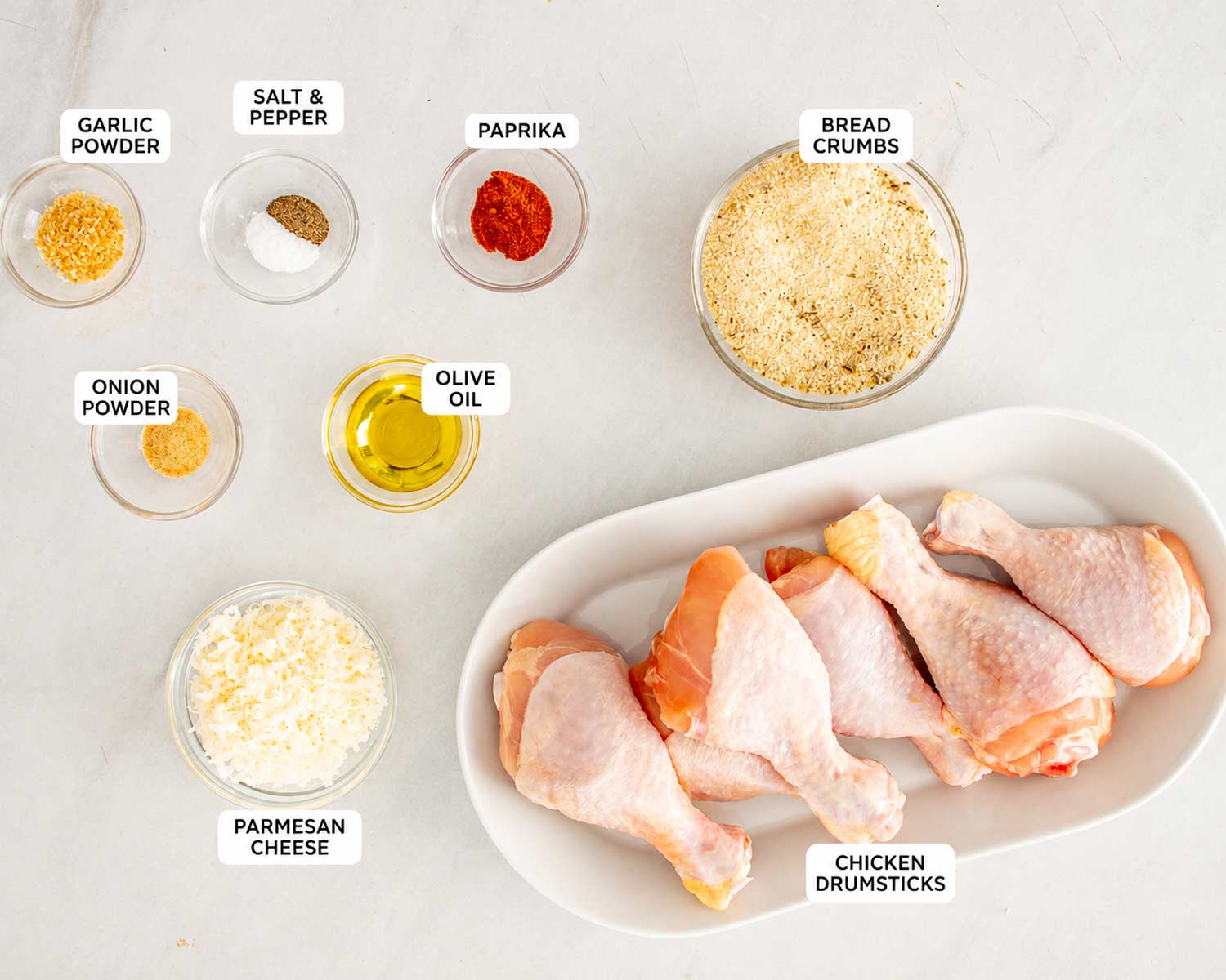 Labeled ingredients for Air Fryer Shake-and-Bake Chicken including drumsticks, breadcrumbs, Parmesan, olive oil, paprika, garlic, onion powder, salt, and pepper.
