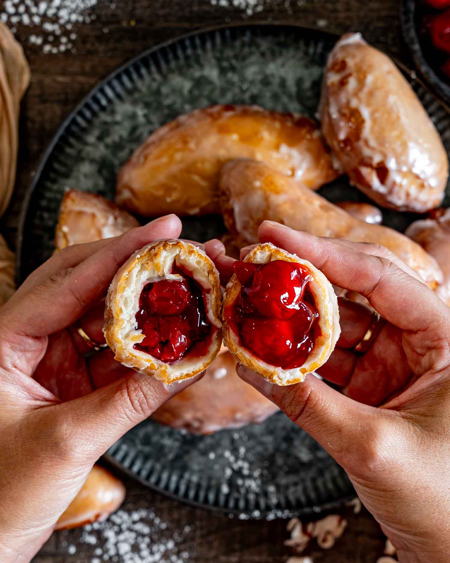 Hands pulling apart a glazed cherry hand pie donut to show the generous, glossy red cherry filling inside.
