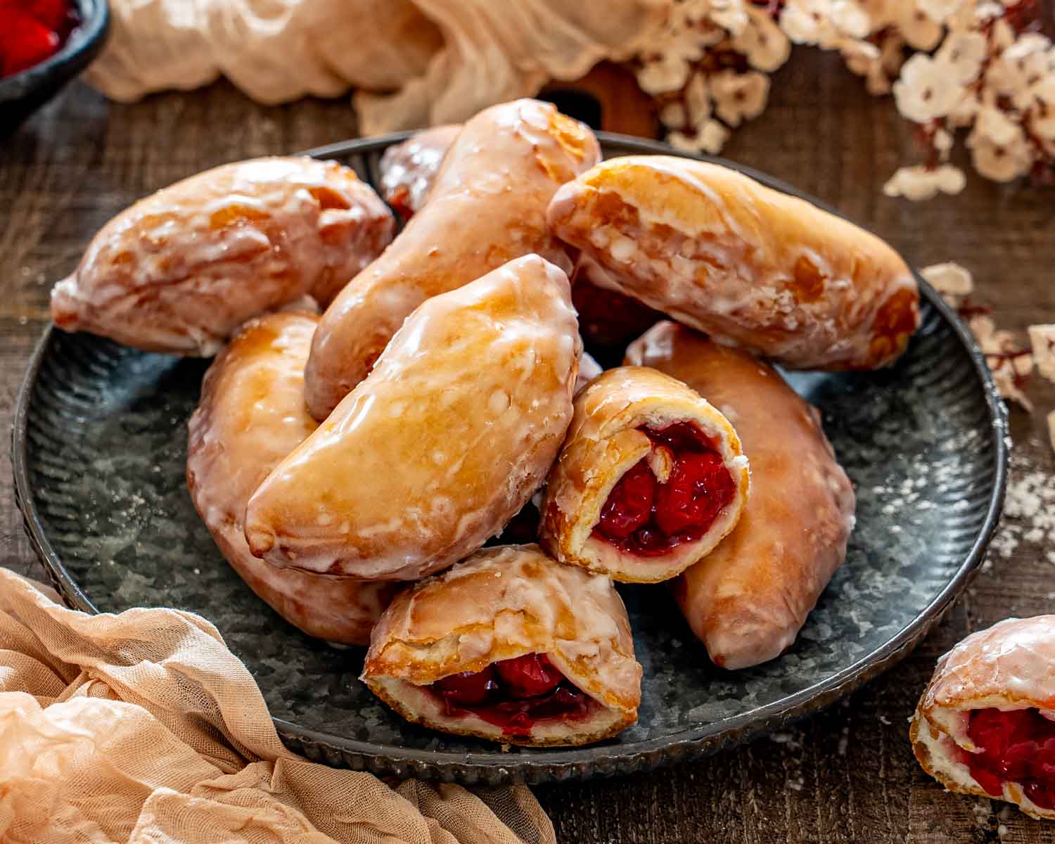 Pile of freshly glazed cherry hand pie donuts on a dark plate, including two pastries cut open.