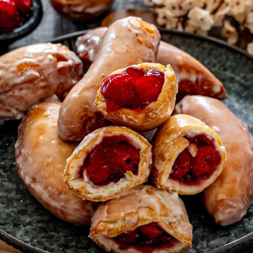 Close-up of glazed cherry hand pie donuts stacked on a plate, with several opened to reveal cherry filling.