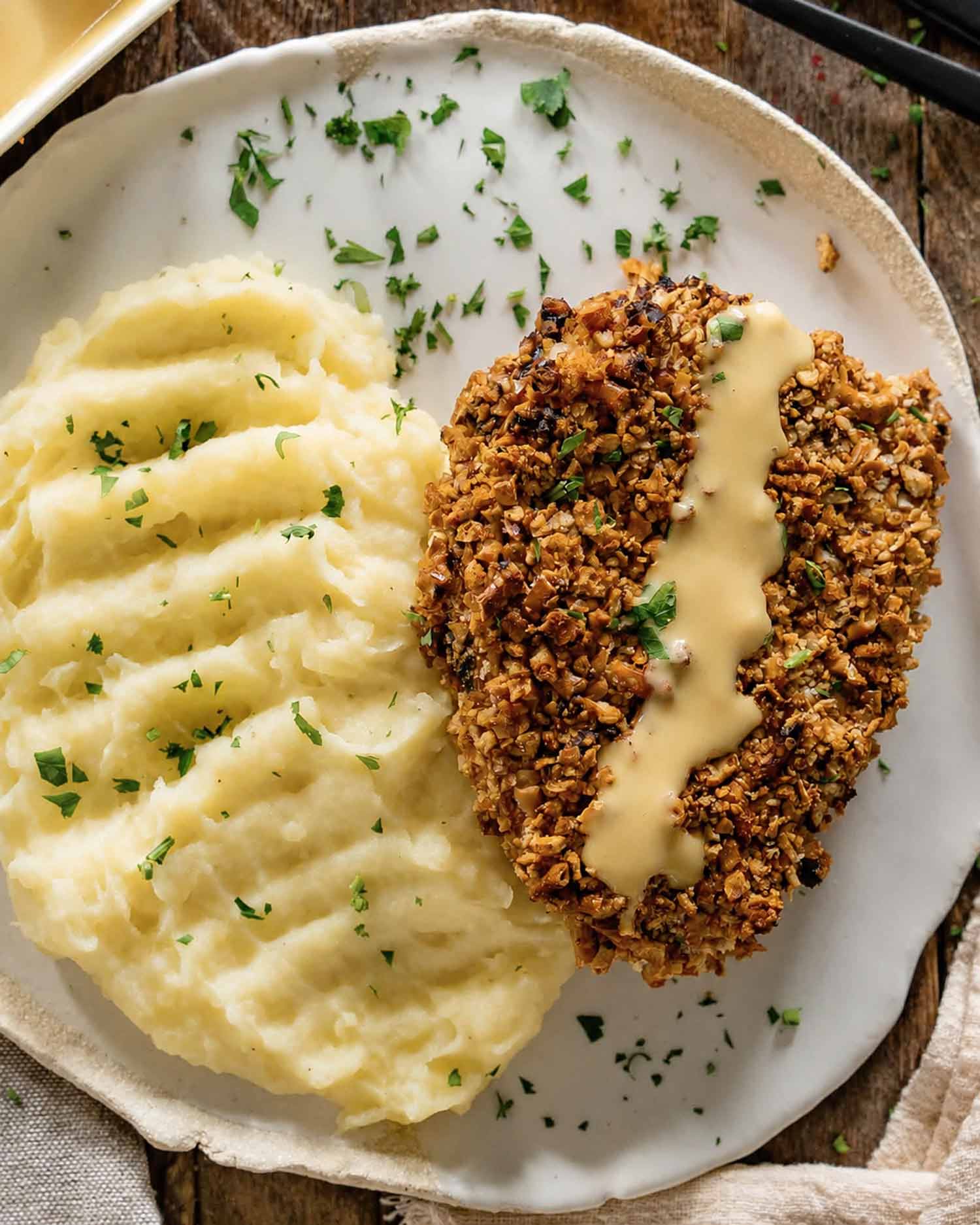 Golden pretzel-crusted pork chop drizzled with honey mustard sits beside creamy mashed potatoes sprinkled with fresh parsley.