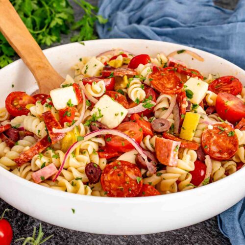 Colorful Italian pasta salad in a white serving bowl with rotini, cured meats, provolone, tomatoes, olives, and fresh parsley.