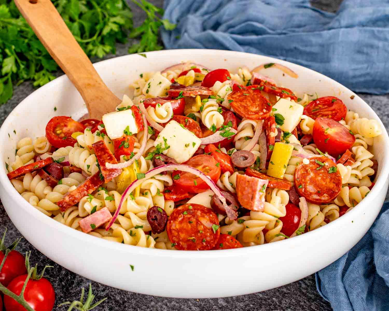 Colorful Italian pasta salad in a white serving bowl with rotini, cured meats, provolone, tomatoes, olives, and fresh parsley.