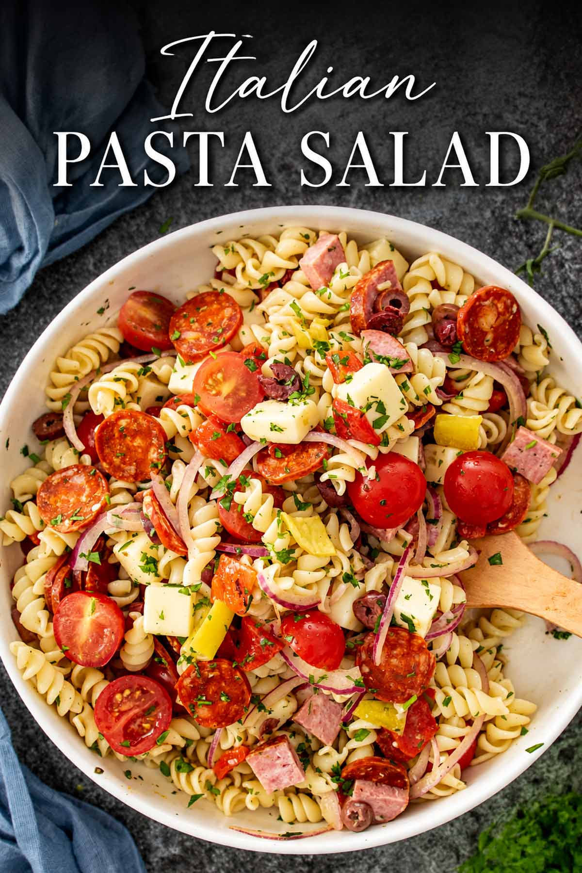 Italian pasta salad loaded with rotini, pepperoni, salami, provolone, tomatoes, olives, and peppers beneath an elegant recipe title.