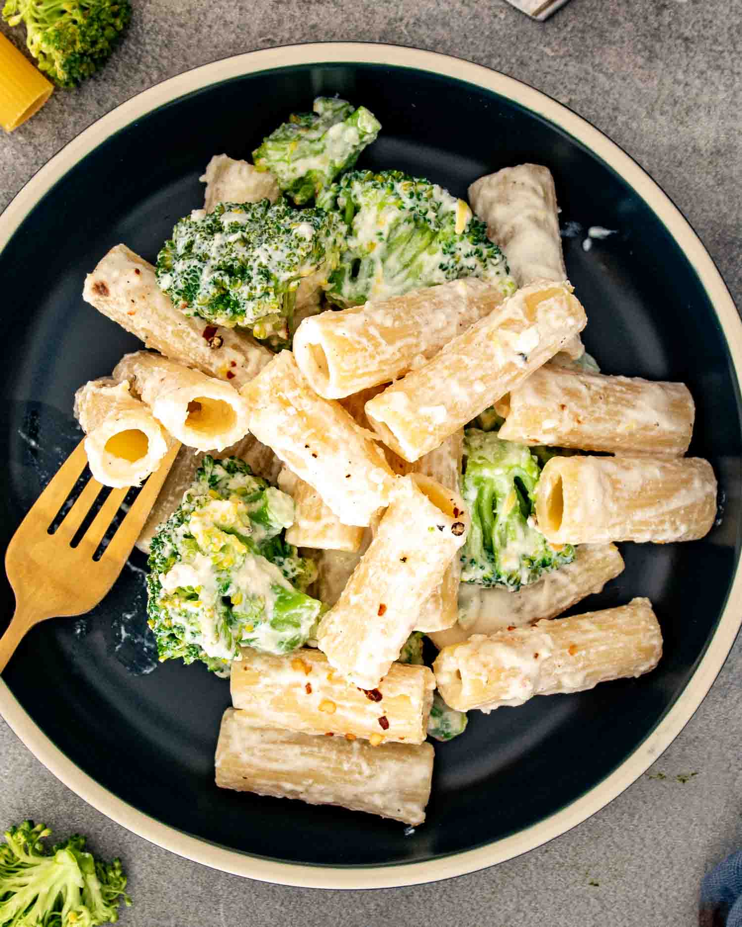 Overhead view of creamy lemon ricotta rigatoni and broccoli in a dark bowl beside a gold fork.