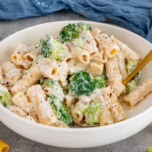 Creamy lemon ricotta rigatoni with broccoli and red pepper flakes served in a white bowl with gold spoon.