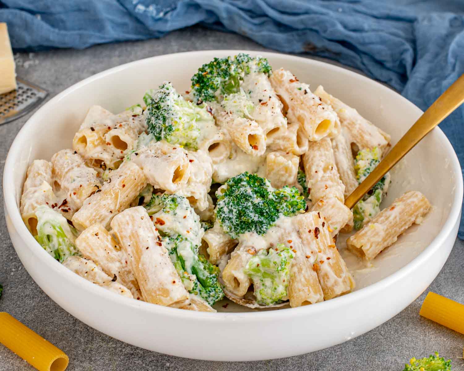 Creamy lemon ricotta rigatoni with broccoli and red pepper flakes served in a white bowl with gold spoon.
