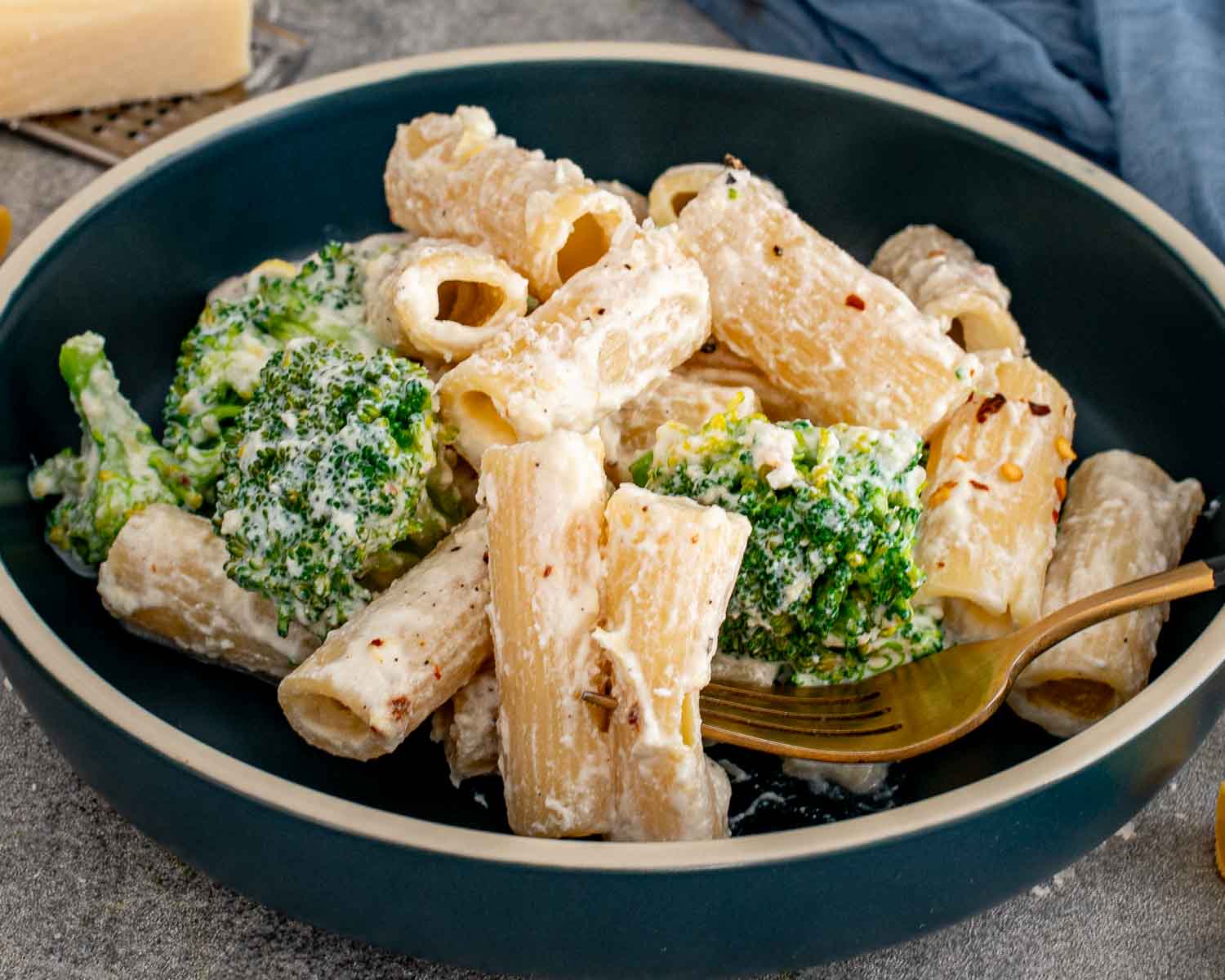 Creamy lemon ricotta rigatoni and broccoli served in a dark bowl with a gold fork and grated Parmesan nearby.