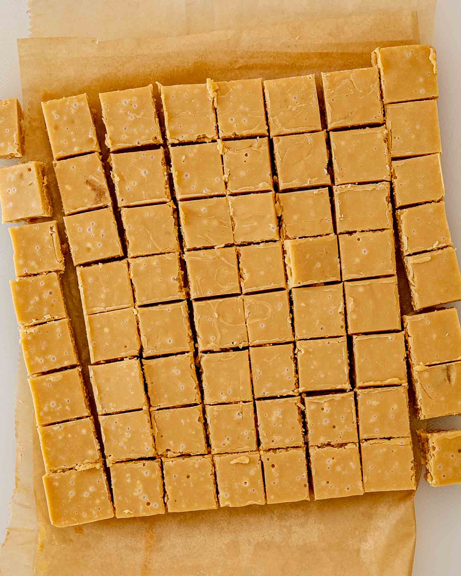 Overhead view of golden maple fudge squares cut into neat rows on parchment paper after cooling completely in the pan.