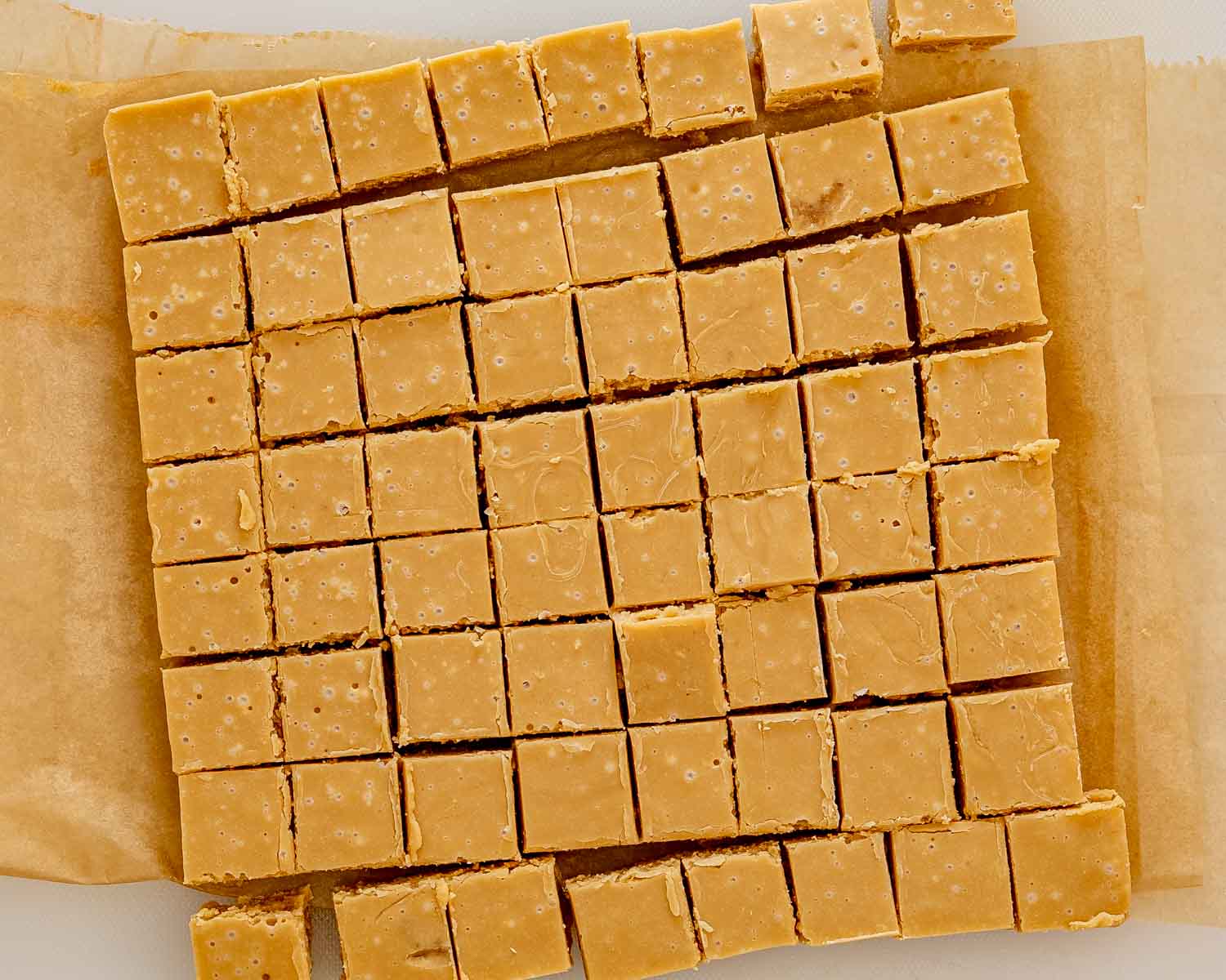 Overhead view of golden maple fudge squares cut into neat rows on parchment paper after cooling completely in the pan.