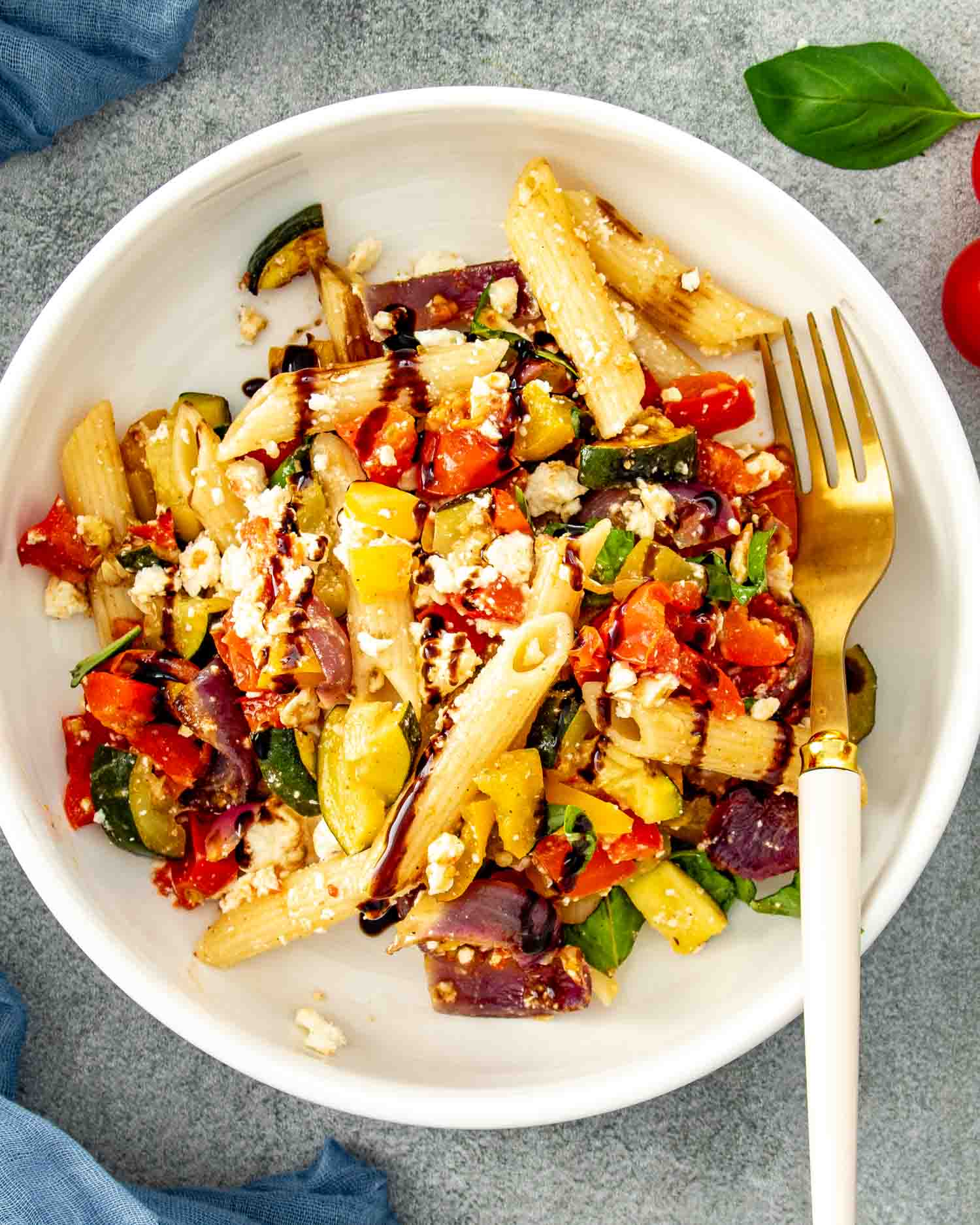 Individual serving of roasted veggie pasta salad with feta and balsamic glaze on a white plate beside a fork.