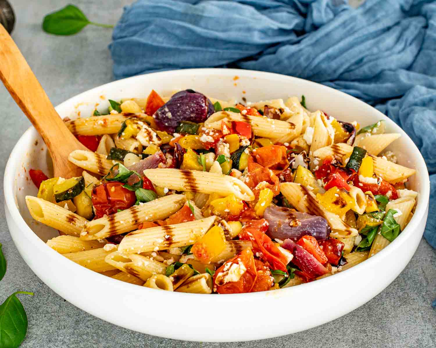 Close view of roasted veggie pasta salad with penne, colorful peppers, zucchini, tomatoes, feta, basil, and balsamic glaze.
