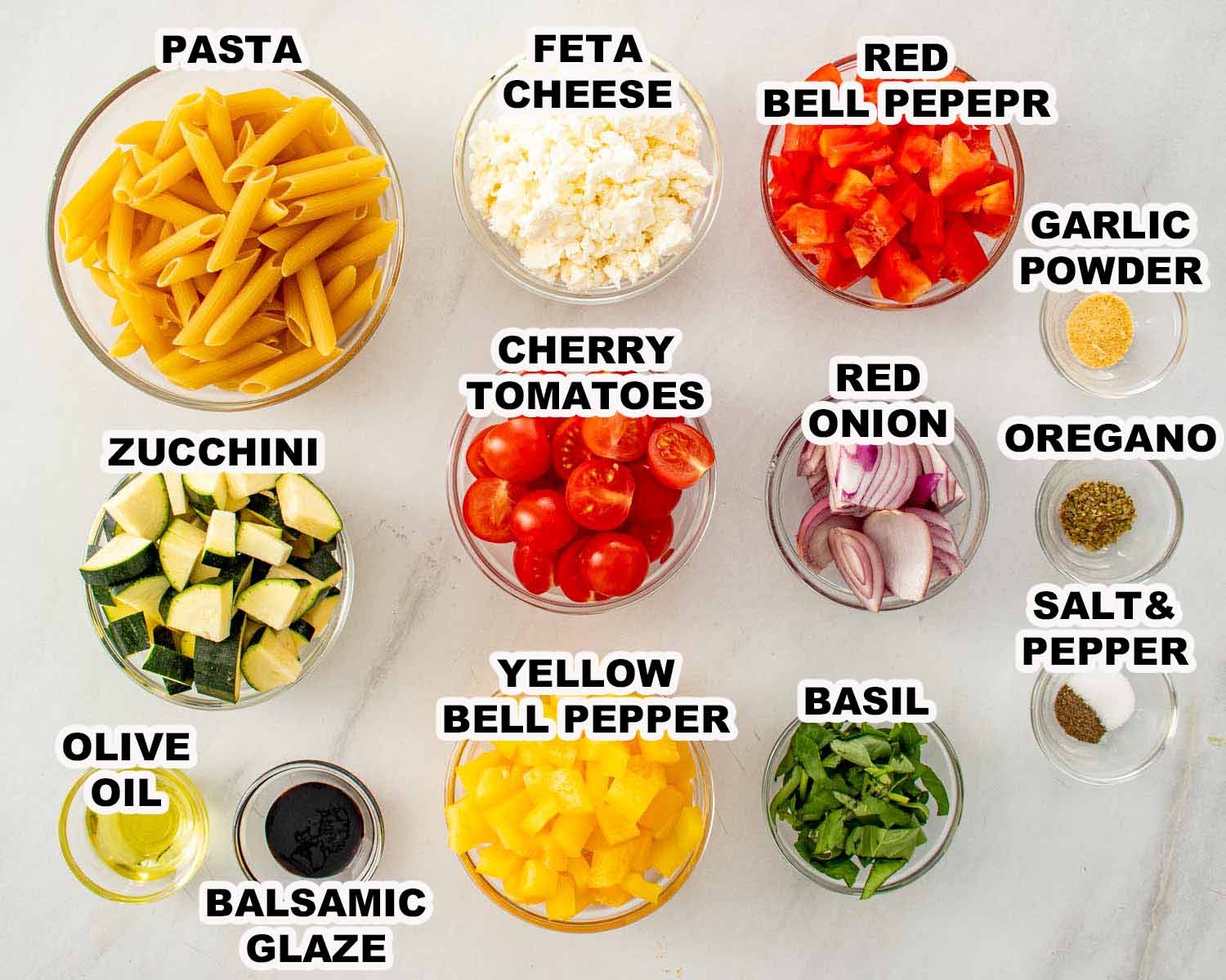 Labeled ingredients for roasted veggie pasta salad, including penne, fresh vegetables, feta, basil, olive oil, and seasonings.