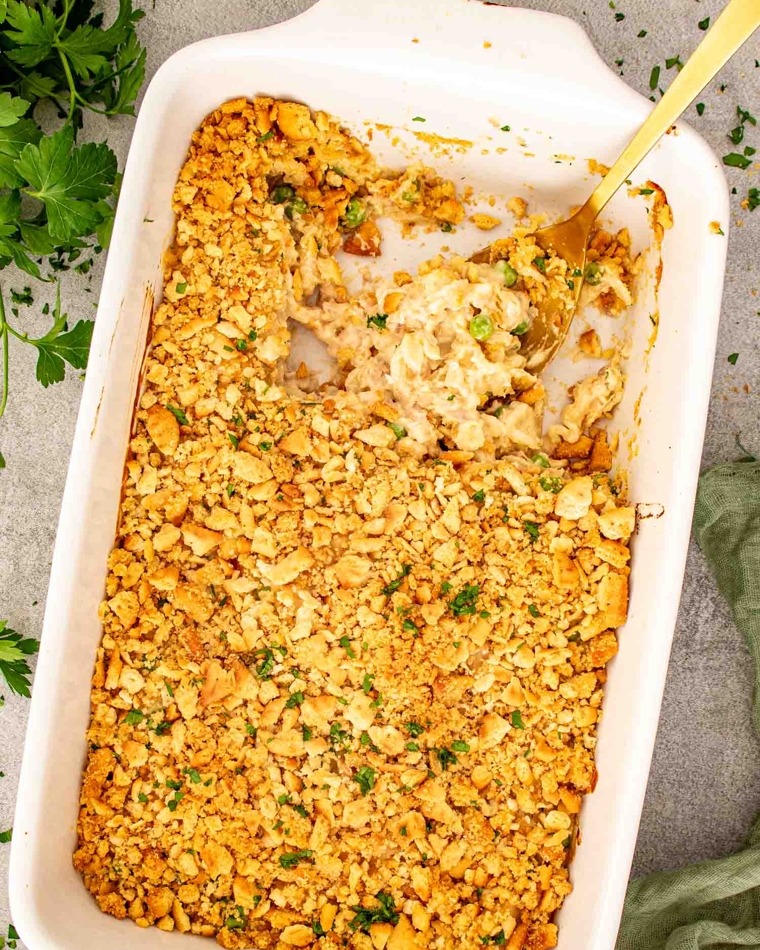 Overhead view of baked tuna noodle casserole in a white dish with a golden spoon and crisp cracker topping.